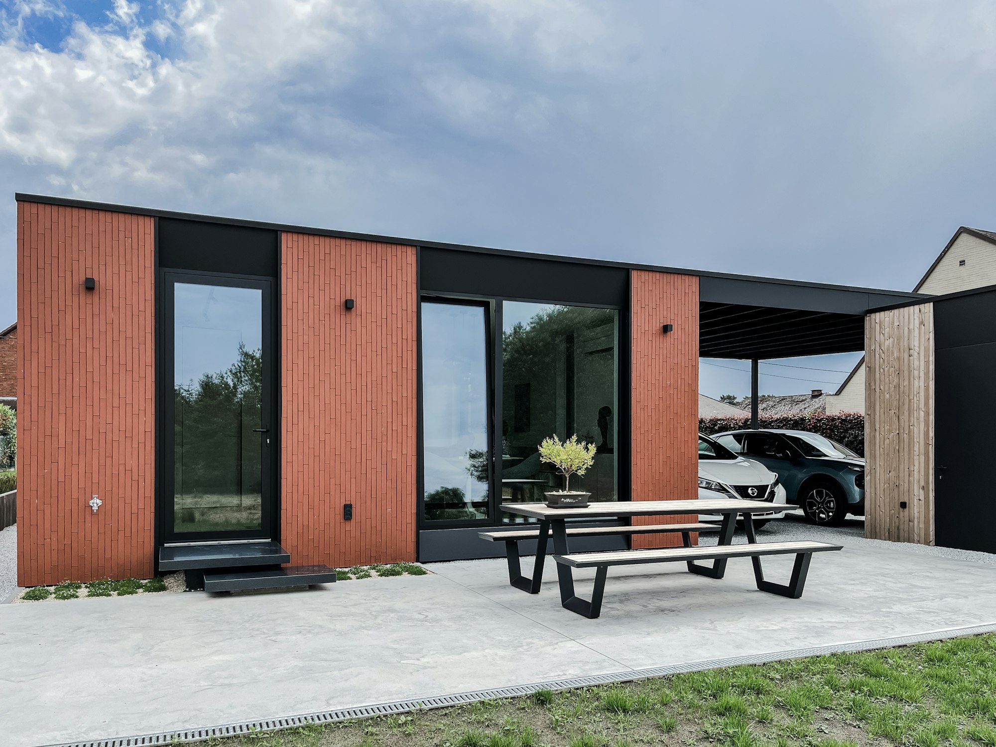 Terras achter een prefab huis van Skilpod in rode steen, carport en tuinberging